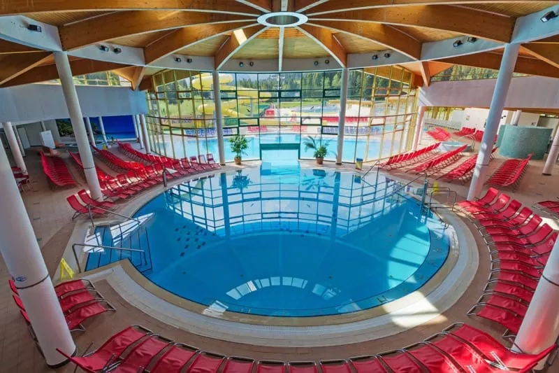 Vnutorny okruhly bazen s cervenymi lehatkami, velke okno na vonkajsi bazen.