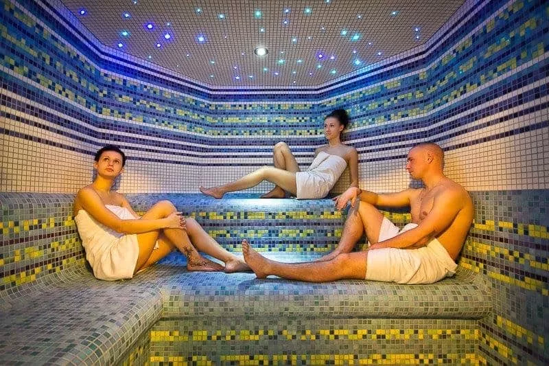 Traja ludia v saune, strop navodzuje dojem hviezd.