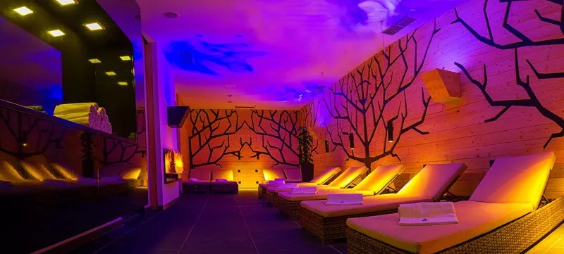 Farebne osvetlena relaxacna zona s lehatkami a uterakmi. Na stenach su nakreslene stromy.