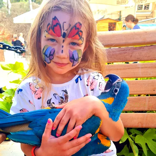 dievca s namalovanou tvarou a papagajom v rukach 